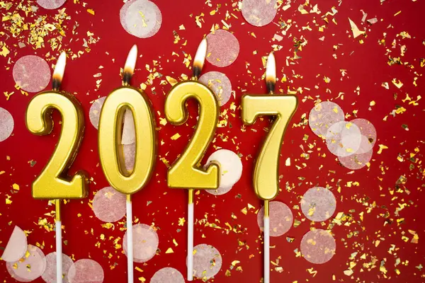 Mutlu yıllar 2027. Tatil geçmişi. 2027 yılının sayıları kırmızı arka planda konfeti ve simle altın mum yakmaktan. Yeni yıl tatili kavramı. Boşluğu kopyala