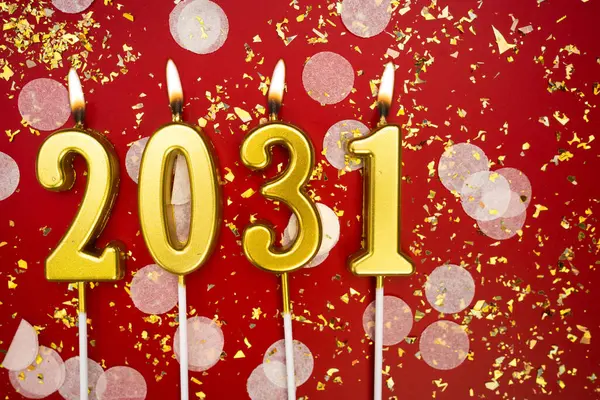 Mutlu yıllar 2031. Tatil geçmişi. 2031 yılının sayıları kırmızı arka planda konfeti ve simle yanan altın mumlardan geliyor. Yeni yıl tatili kavramı. Boşluğu kopyala