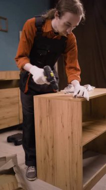 Mavi tulumlu profesyonel montaj işçisi marangozluk işinde elektrikli matkap kullanarak ahşap mobilya montajı yapıyor. Mobilya döşemesi. Boşluğu kopyala