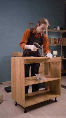 Mavi tulumlu profesyonel montaj işçisi marangozluk işinde elektrikli matkap kullanarak ahşap mobilya montajı yapıyor. Mobilya döşemesi. Boşluğu kopyala