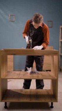 Mavi tulumlu profesyonel montaj işçisi marangozluk işinde elektrikli matkap kullanarak ahşap mobilya montajı yapıyor. Mobilya döşemesi. Boşluğu kopyala