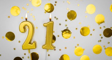 Beyaz arka planda, altın konfeti ve simle 21 numaralı yanan doğum günü mumu. Yirmi bir yaşında. Doğum günün kutlu olsun. Geçmiş şenliği kartı. Bayrak