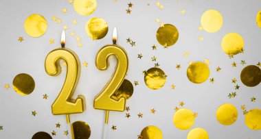 Beyaz arka planda, altın konfeti ve simle 22 numaralı yanan doğum günü mumu. Yirmi iki yaşında. Doğum günün kutlu olsun. Geçmiş şenliği kartı. Bayrak