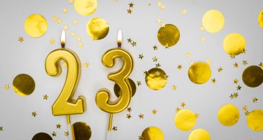 Beyaz arka planda, altın konfeti ve simle 23 numaralı yanan doğum günü mumu. Yirmi üç yaşında. Doğum günün kutlu olsun. Geçmiş şenliği kartı. Bayrak