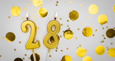 Beyaz arka planda, altın konfeti ve simle 28 numaralı yanan doğum günü mumu. Yirmi sekiz yaşında. Doğum günün kutlu olsun. Geçmiş şenliği kartı. Bayrak