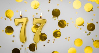 77 numara konfeti arkaplanlı beyaz üzerine doğum günü mumu. Yetmiş yedi yıllık doğum günü. Doğum günü ve yıldönümü kutlaması kavramı. Boşluğu kopyala