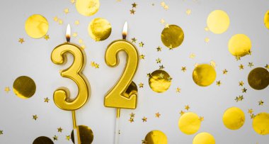 Beyaz arka planda, altın konfeti ve simle birlikte 32 numaralı yanan doğum günü mumu. Otuz iki yaşında. Doğum günün kutlu olsun. Geçmiş şenliği kartı. Bayrak