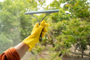 Cam temizleyicisinin yakın plan sarı eldiven temizleme penceresinde cam sileceği ve silecekle. Ev işleri ve ev işleri konsepti