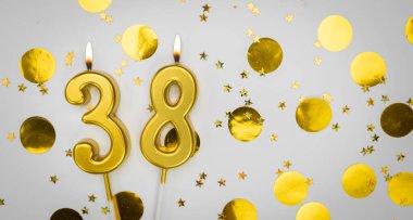 38 numaralı yanan doğum günü mumu beyaz arka planda altın konfeti ve sim ile. Otuz sekiz yaşında. Doğum günün kutlu olsun. Geçmiş şenliği kartı. Bayrak
