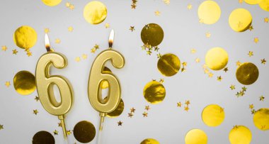 66 numaralı doğum günü mumu beyaz üzerine konfeti arkaplanlı. Altmış altı yıllık doğum günü. Doğum günü ve yıldönümü kutlaması kavramı. Boşluğu kopyala