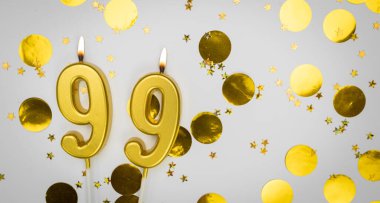 99 numaralı doğum günü mumu beyaz üzerine konfeti arkaplanlı. Doksan dokuz yıllık doğum günü. Doğum günü ve yıldönümü kutlaması kavramı. Boşluğu kopyala.