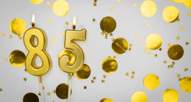 85 numaralı doğum günü mumu beyaz üzerine konfeti arkaplanlı. Seksen beş yıllık doğum günü. Doğum günü ve yıldönümü kutlaması kavramı. Boşluğu kopyala.