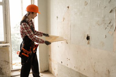 Tamirci, duvardaki eski duvar kağıtlarını kaldırıyor. Odayı yenileme için hazırlıyor. İnşaat ve yenileme konsepti