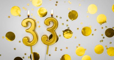 33 numaralı yanan doğum günü mumu beyaz arka planda altın konfeti ve sim ile. Otuz üç yaşında. Doğum günün kutlu olsun. Geçmiş şenliği kartı. Bayrak