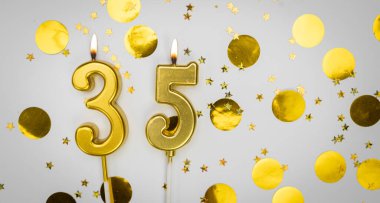 35 numaralı yanan doğum günü mumu beyaz arka planda altın konfeti ve sim ile. Otuz beş yaşında. Doğum günün kutlu olsun. Geçmiş şenliği kartı. Bayrak