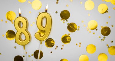 89 numaralı doğum günü mumu beyaz üzerine konfeti arkaplanlı. Seksen dokuz yıllık doğum günü. Doğum günü ve yıldönümü kutlaması kavramı. Boşluğu kopyala.