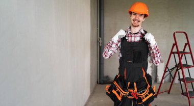 İnşaattaki inşaatçı zaferi kutluyor ve gri duvara karşı ayakta duruyor. Banner, boşluğu kopyala