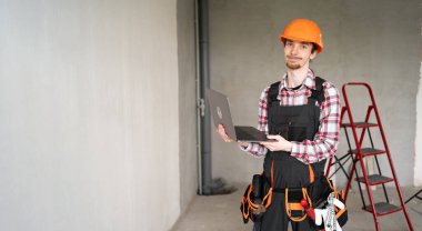 İnşaat alanında dizüstü bilgisayarı olan inşaatçı ya da ustabaşı kamerada arkadaş canlısı görünen bir bilgisayarda çalışıyor. Boşluğu kopyala