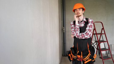 Güvenlik kaskı takan düşünceli müteahhit yenileme sırasında yeni bir dairede durmayı düşünüyor. Pankart. Boşluğu kopyala