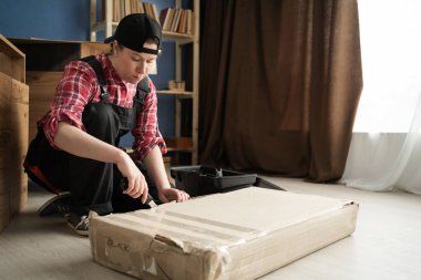 Kadın tamirci, yerde montaj için yeni mobilyalarla dolu kutuları açıyor. Boşluğu kopyala