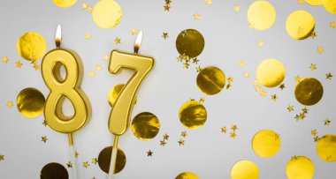 87 numaralı doğum günü mumu beyaz üzerine konfeti arkaplanlı. Seksen yedi yıllık doğum günü. Doğum günü ve yıldönümü kutlaması kavramı. Boşluğu kopyala.