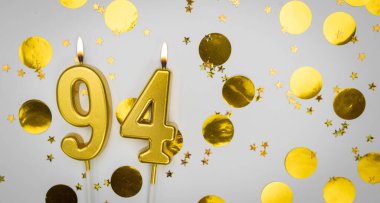 94. doğum günü mumu beyaz üzerine konfeti arkaplanlı. Doksan dört yıllık doğum günü. Doğum günü ve yıldönümü kutlaması kavramı. Boşluğu kopyala.