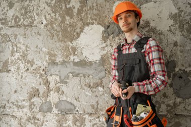 İnşaat alanında çalışan kasketli yakışıklı genç inşaatçı eski duvar arkasında duruyor. Boşluğu kopyala