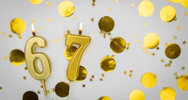 67 numaralı doğum günü mumu beyaz üzerine konfeti arkaplanlı. Altmış yedi yıllık doğum günü. Doğum günü ve yıldönümü kutlaması kavramı. Boşluğu kopyala