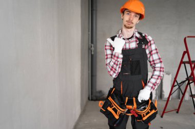 İnşaat işçisi sarı miğferli, inşaat alanında duran mesaj ya da reklam için başparmağıyla mekanı işaret ediyor. Boşluğu kopyala