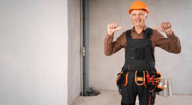 Güvenlik kaskı takmış, gülümseyen ve parmaklarıyla kendini gösteren olgun bir erkek müteahhit. meslek, inşaat ve inşaat kavramı