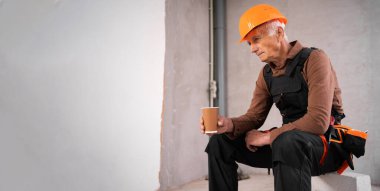 İşten sonra şantiyede kahve molası veren yorgun kıdemli inşaat işçisi. Pankart. Boşluğu kopyala