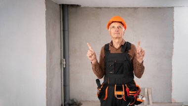 Yaşlı inşaatçı ya da inşaat işçisi boş alanı parmaklarıyla işaret ediyor. İnşaat alanı ve inşaat konsepti