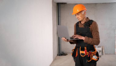 Foreman veya müteahhit inşaat alanında teknolojiyle çalışan dizüstü bilgisayarla kask takıyor. - Sancak. Boşluğu kopyala