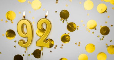 92 numaralı doğum günü mumu beyaz üzerine konfeti arkaplanlı. Doksan iki yıllık doğum günü. Doğum günü ve yıldönümü kutlaması kavramı. Boşluğu kopyala.