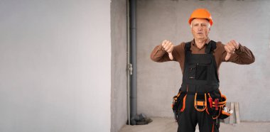 Güvenlik kaskı takmış yaşlı erkek müteahhit hoşlanmadığı için başparmak gösteriyor. Meslek, inşaat ve inşaat konsepti. Pankart. Boşluğu kopyala