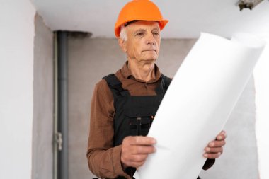 Yaşlı erkek müteahhit, yeni ev planı üzerinde çalışıyor, inşaat sahasında belgelerle çalışıyor. Boşluğu kopyala