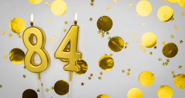 84 numaralı doğum günü mumu beyaz üzerine konfeti arkaplanlı. Seksen dört yıllık doğum günü. Doğum günü ve yıldönümü kutlaması kavramı. Boşluğu kopyala.