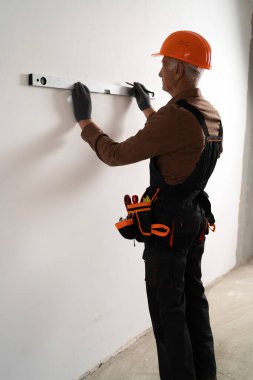 Emekli inşaatçı, yenilendikten sonra yeni evdeki ruh seviyesini ölçmek için duvar kullanıyor. Dikey görünüm. Boşluğu kopyala