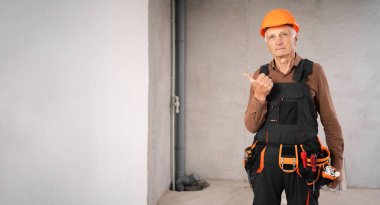 Güvenlik kaskı takmış yaşlı erkek müteahhit şuraya bakın diyor. Boş alanı işaret eden bir parmak. Meslek, inşaat ve inşaat konsepti. Boşluğu kopyala