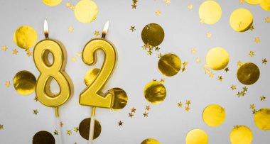 82 numaralı doğum günü mumu beyaz üzerine konfeti arkaplanlı. Seksen iki yıllık doğum günü. Doğum günü ve yıldönümü kutlaması kavramı. Boşluğu kopyala.