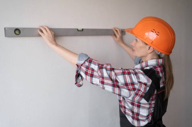 Turuncu şapka takan kadın inşaat işçisi duvarları ruh seviyesiyle ölçüyor. Boşluğu kopyala