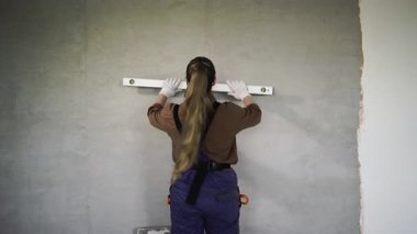 Tamirci kadın beyaz duvarda ruh seviyesinde aletlerle ölçüm yapıyor. Arkadan bak. Boşluğu kopyala