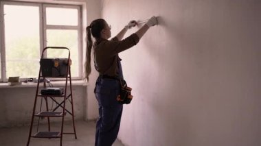 DIY ev geliştirme konsepti. Kadın tamirci bir metre tutuyor, duvarları ölçüyor. Boşluğu kopyala