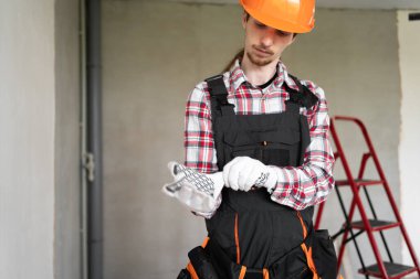 İnşaat işçisi ya da genç inşaatçı, tadilat için evde dururken eldivenlerini takıyor. Boşluğu kopyala