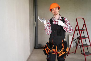 Yeni ürün için avuç içi açık tutan genç inşaatçı inşaat alanında fotokopi alanı ile kol kola işaret ediyor. Boşluğu kopyala