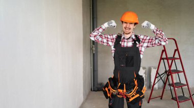 İnşaatçı adam kollarını kaldırır ve inşaat alanında ya da yeni evde çalışan pazılarını gösterir. Kaslarıma bak. Pankart. Boşluğu kopyala