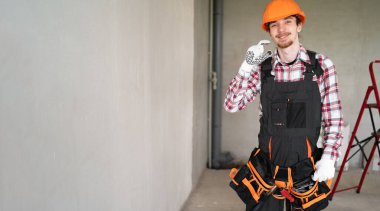 Güvenlik kaskı takan genç müteahhit inşaat alanında parmaklarıyla el hareketleriyle hareket ediyor. Pankart. Boşluğu kopyala