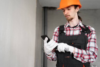 Akıllı telefonu olan bir inşaatçı. İnşaat işçisi inşaat işçisi. İnşaatçıya şapka ve üniforma giyiyor. Boşluğu kopyala