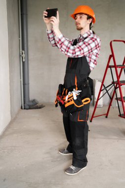 Akıllı telefonlu genç inşaatçı cep kamerasıyla fotoğraf çekiyor. İnşaat işi ve inşaat konsepti