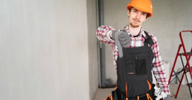 İnşaat alanında miğfer takan üzgün müteahhit ya da müteahhit, baş parmağından hoşlanmadığı jestler yapıyor. Pankart. Boşluğu kopyala